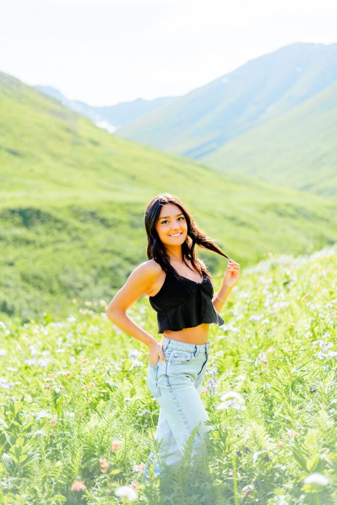 girl standing in flower field with mountains behind her at Hatcher Pass