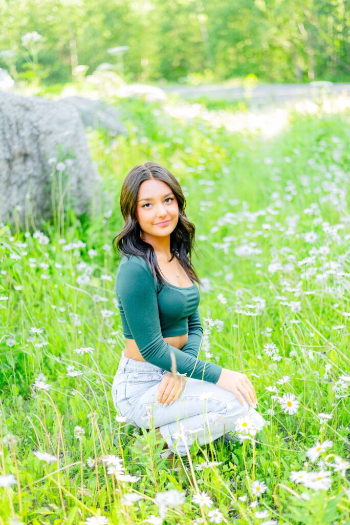 Girl squatting in field of flowers with rocks behind her at Hatcher Pass