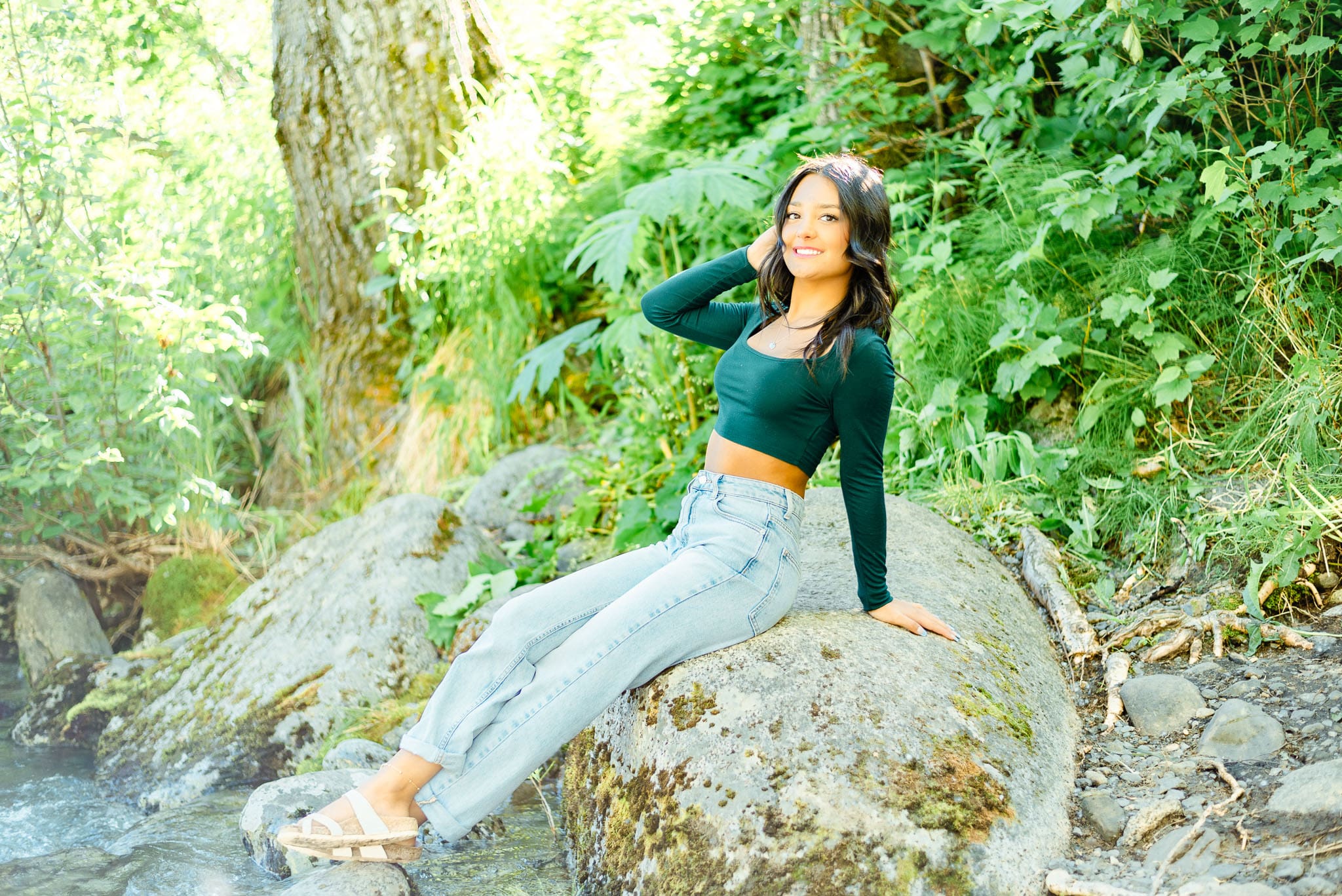 girl sitting on a rock with greenery and trees behind her